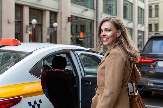 beautiful young woman gets into yellow taxi city smiling blonde beige coat travel traffic metropolis 120897 3659